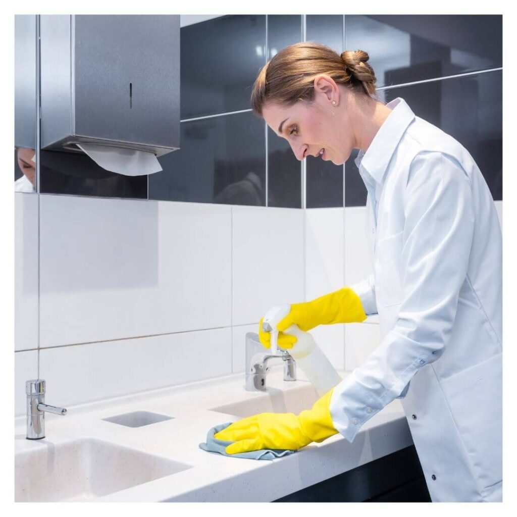 woman wearing cloves wipes down business bathroom counter